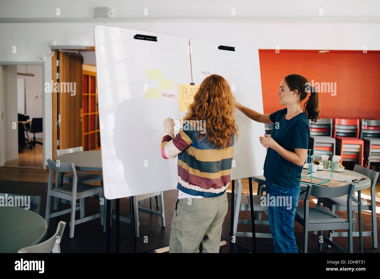 Confident female technicians discussing project over whiteboard at creative office Stock Photo