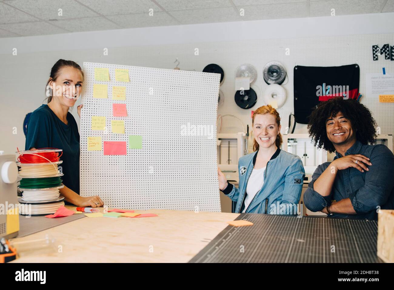 Portrait of smiling multi-ethnic technicians with adhesive notes on pegboard at creative office Stock Photo