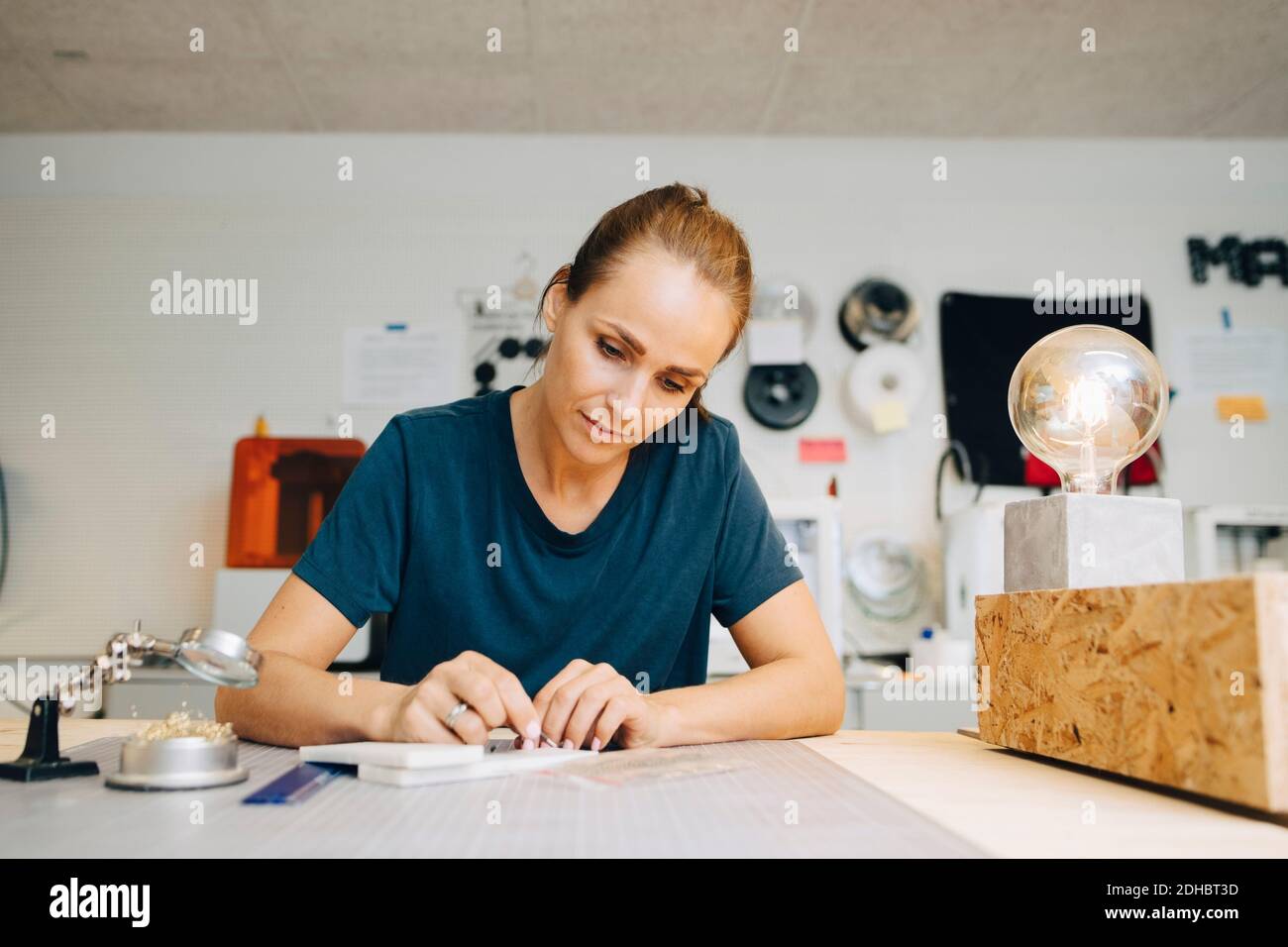 Confident female technician working at workbench while sitting in creative office Stock Photo