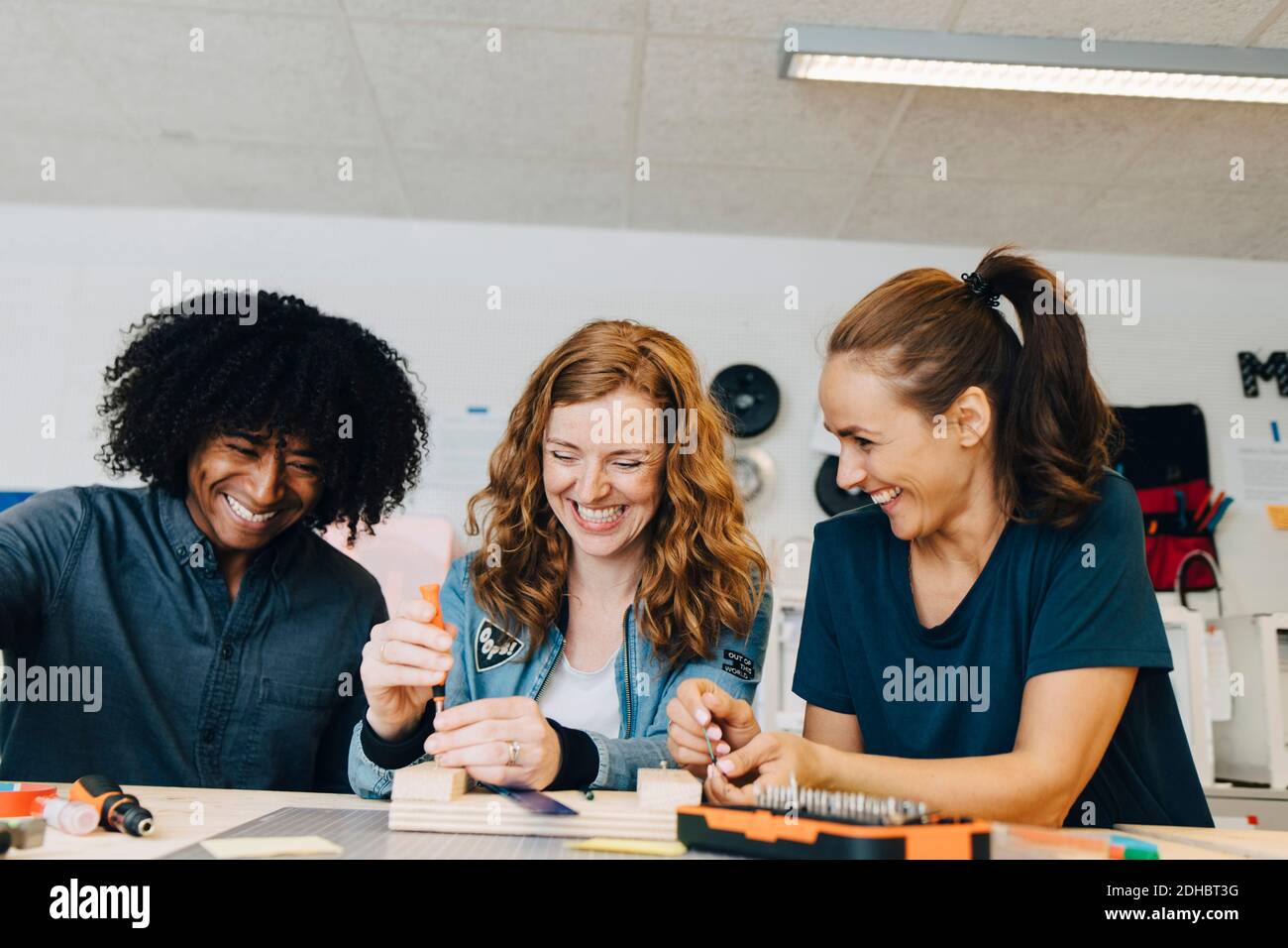 Smiling multi-ethnic technicians working on wood at workbench in creative office Stock Photo