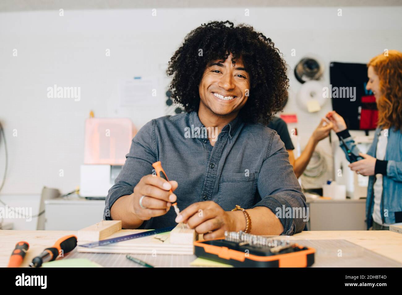 Portrait of smiling male technician using tool on wood at workbench in creative office Stock Photo