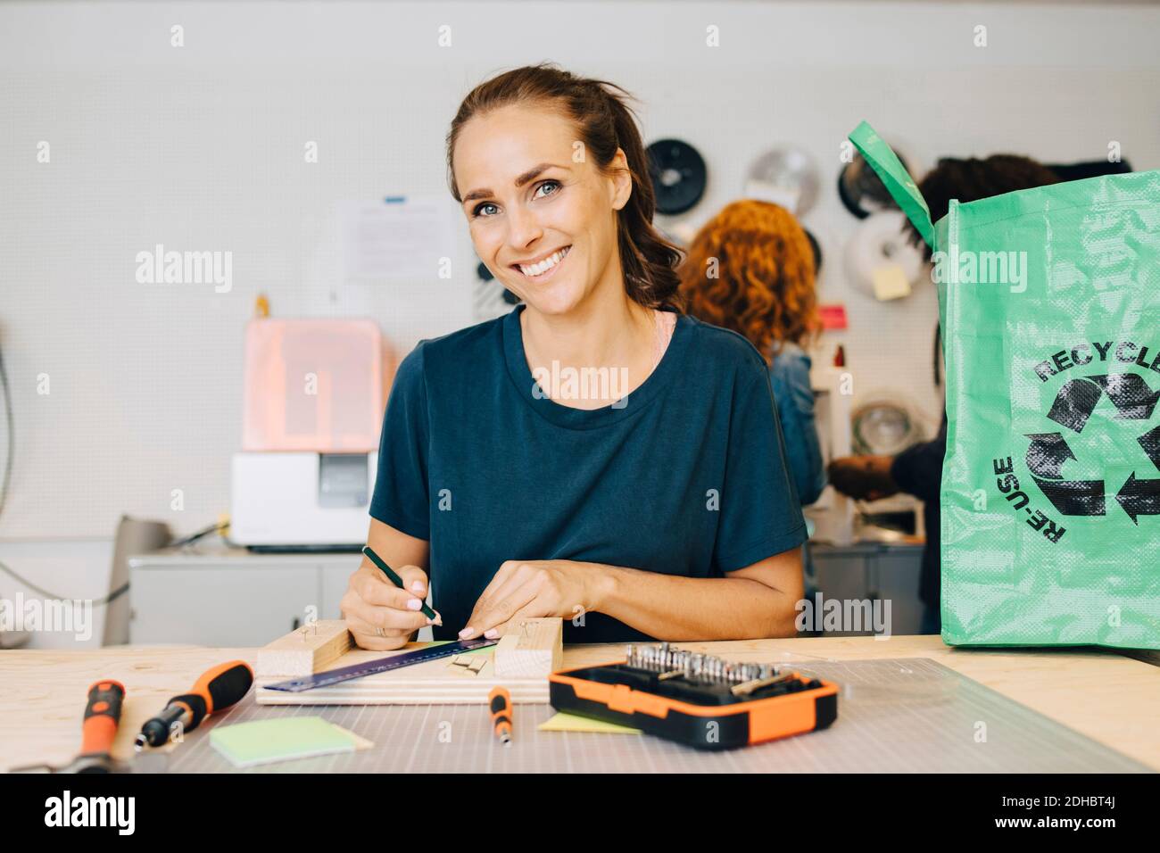 Portrait of smiling female technician working while sitting at workbench in creative office Stock Photo