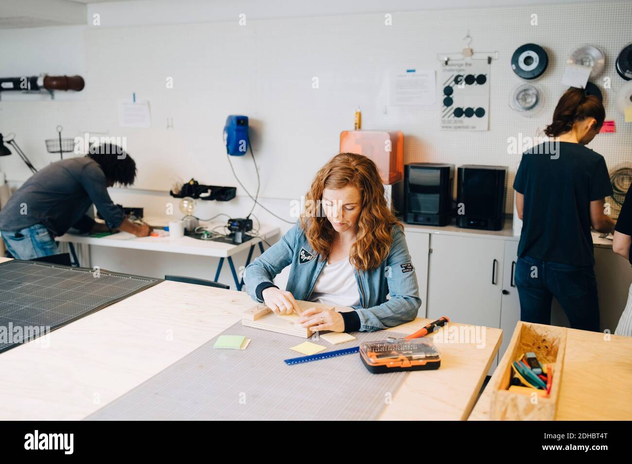 Confident female technician working on wood at workbench with colleagues in office Stock Photo