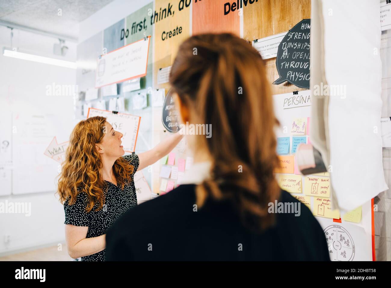 Rear view of businesswoman looking at female colleagues discussing over strategy on wall at creative office Stock Photo