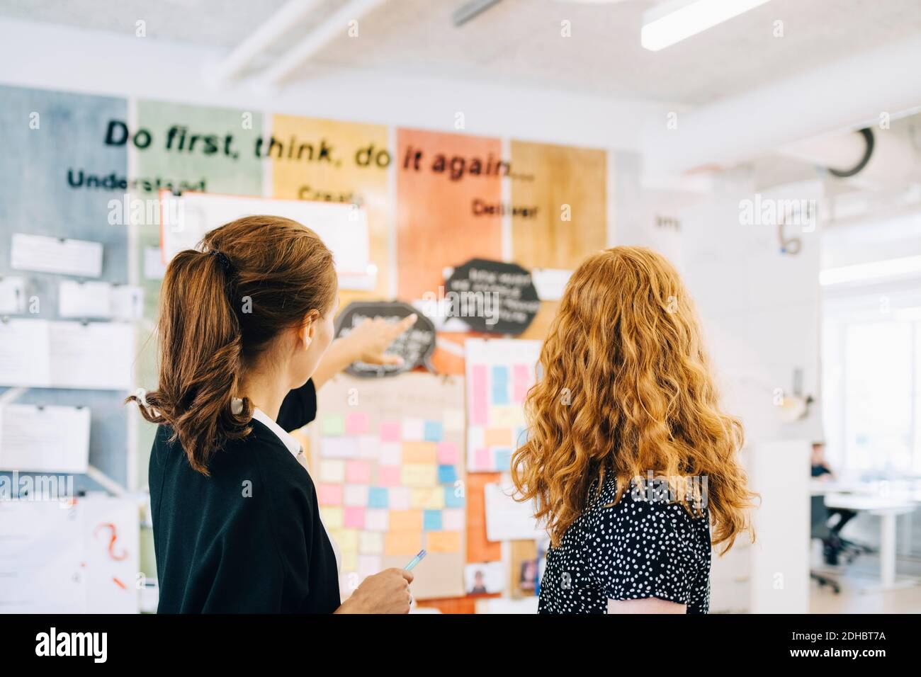 Confident female colleagues discussing over strategy on wall at creative office Stock Photo