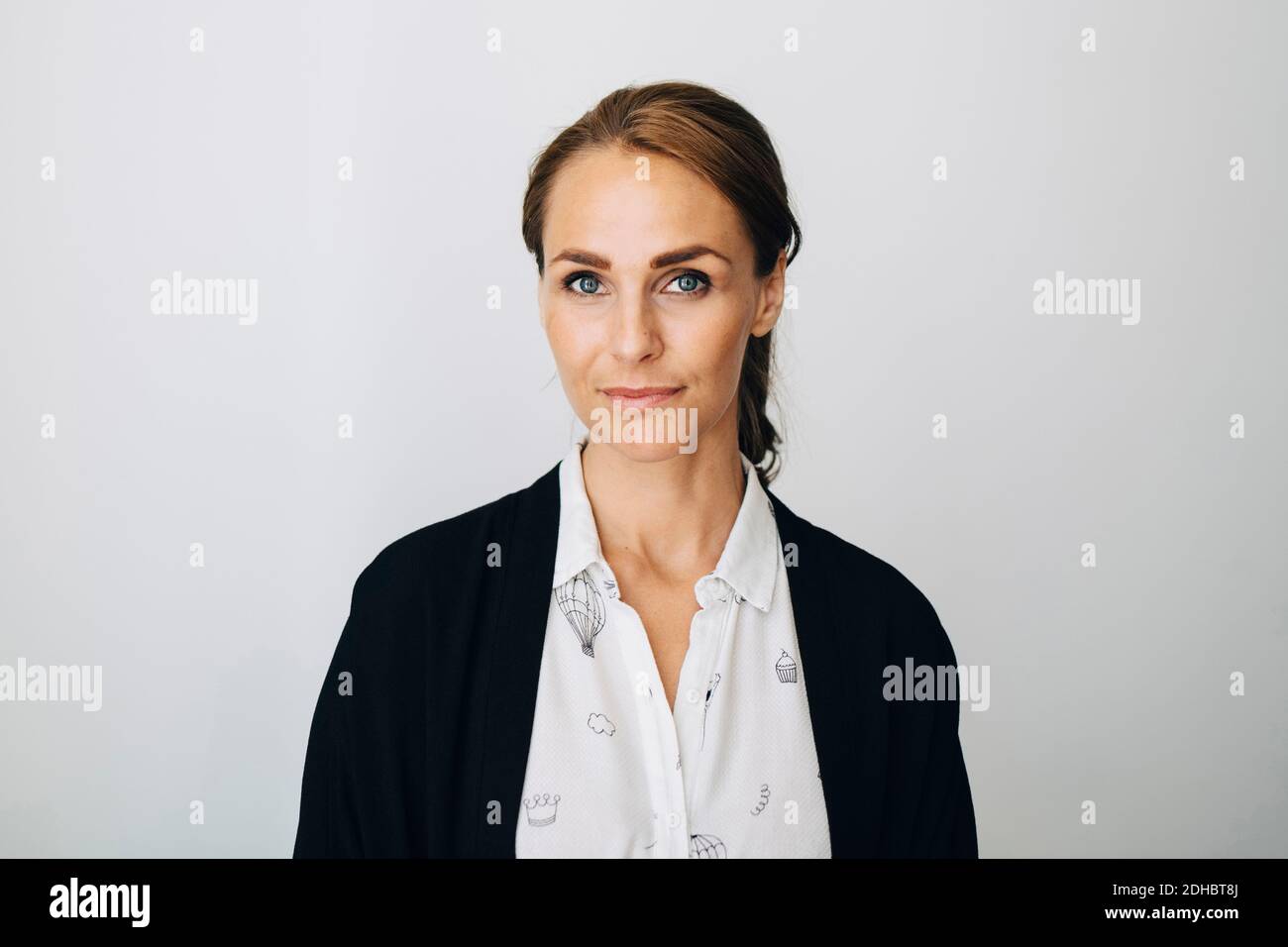 Portrait of confident mid adult businesswoman standing against white wall at creative office Stock Photo