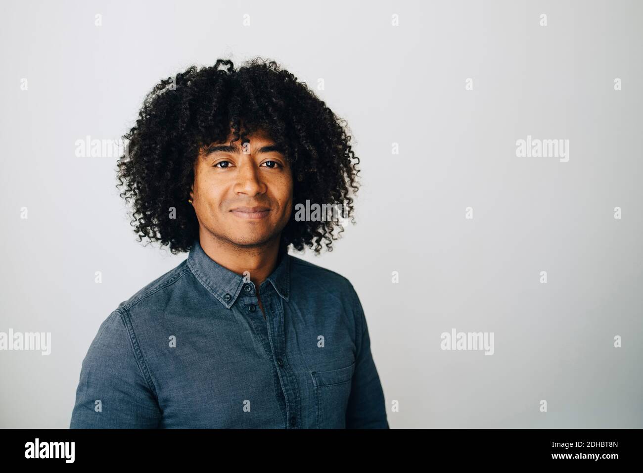Portrait of confident businessman with curly hair standing against white wall at creative office Stock Photo