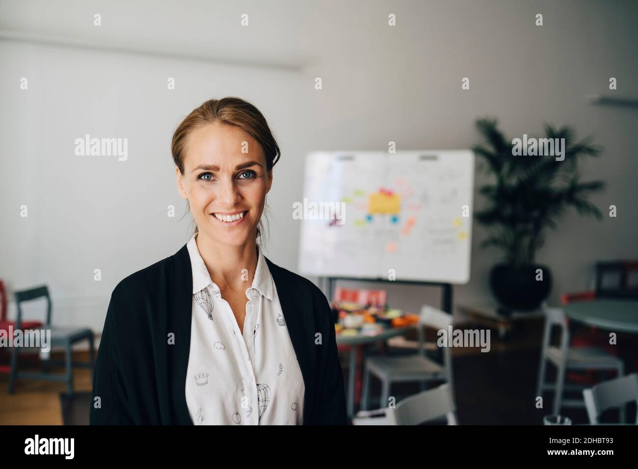 Portrait of smiling mid adult businesswoman standing at creative office Stock Photo