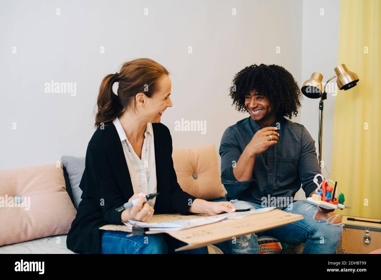 Smiling multi-ethnic business colleagues discussing over placard while sitting on sofa in lobby at creative office Stock Photo
