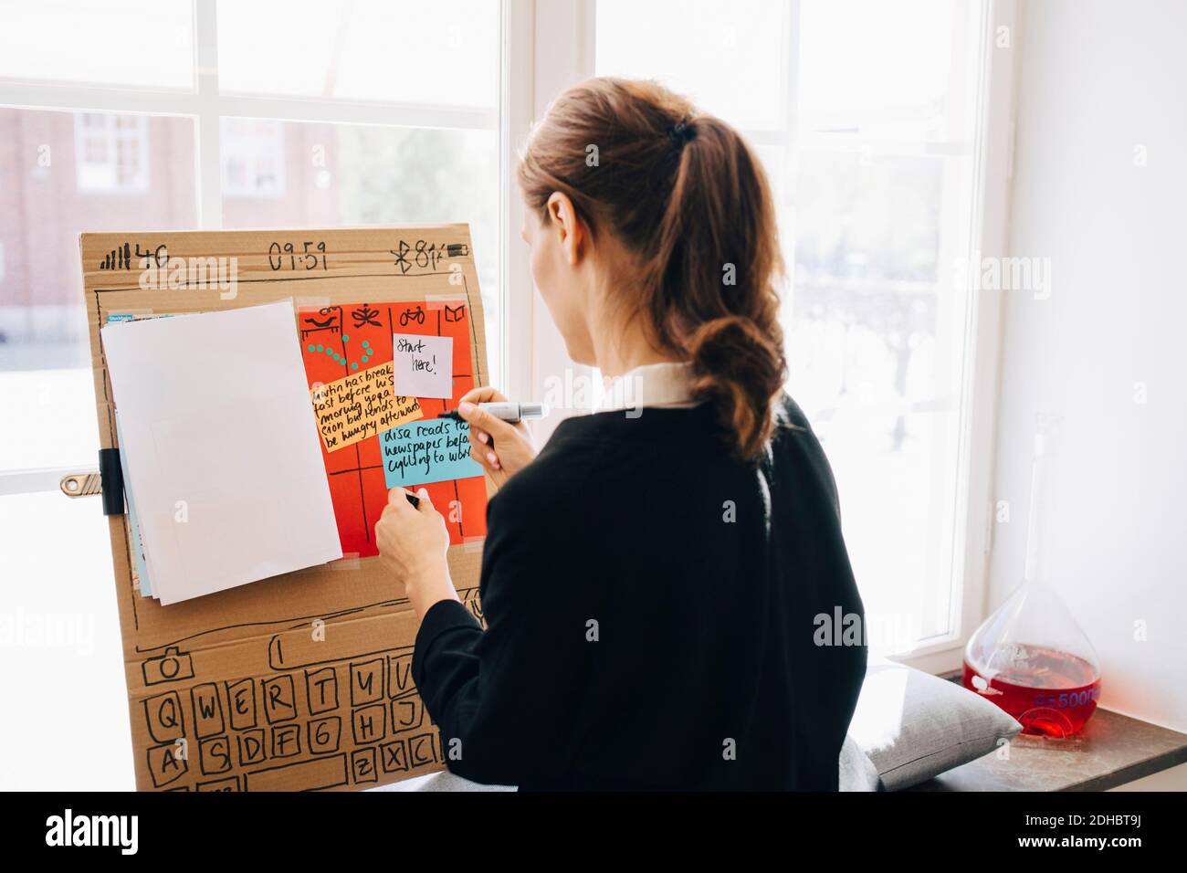 Rear view of businesswoman writing strategy on placard against window at creative office Stock Photo