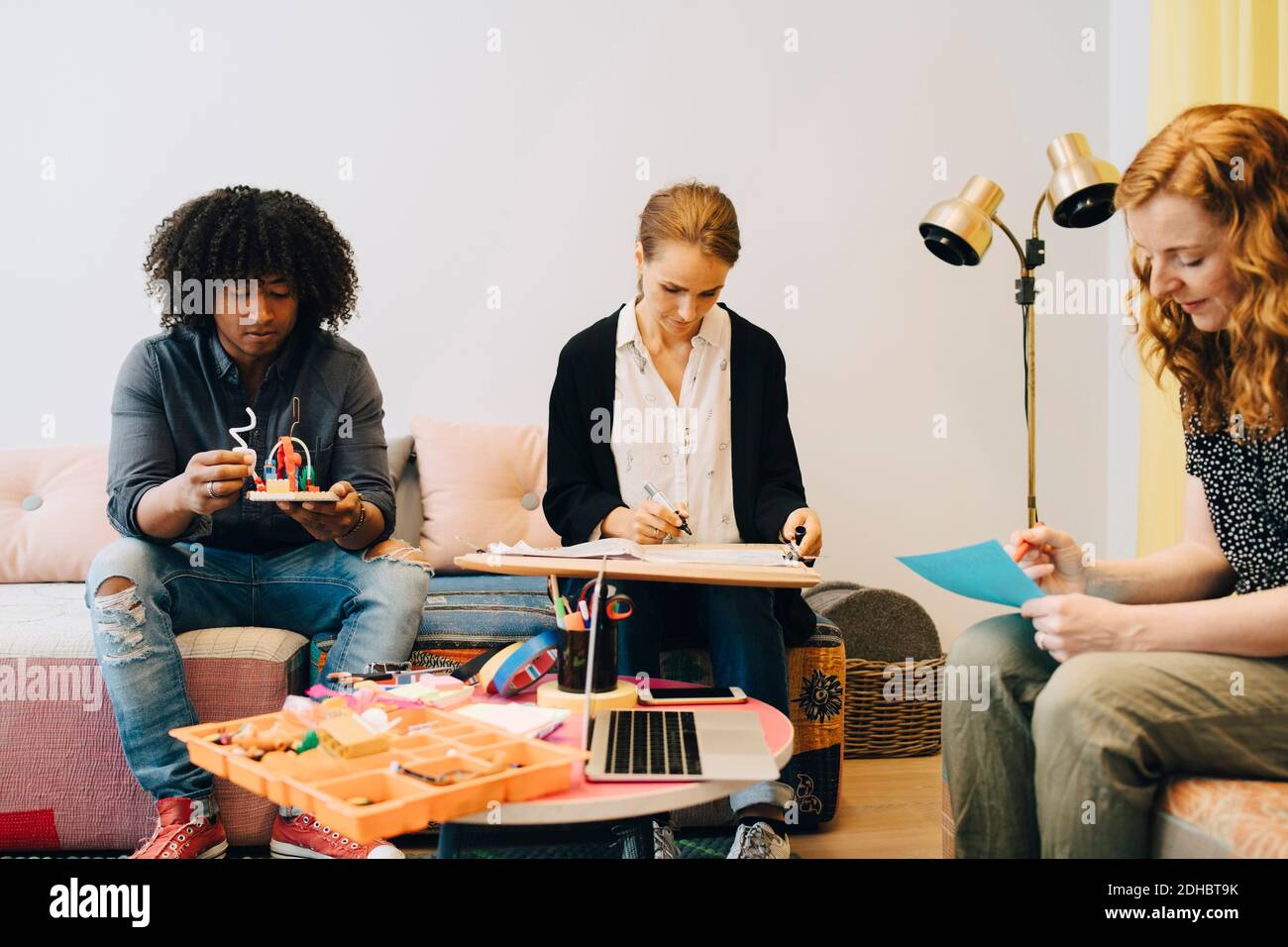 Multi-ethnic business colleagues working while sitting on sofa in lobby at creative office Stock Photo