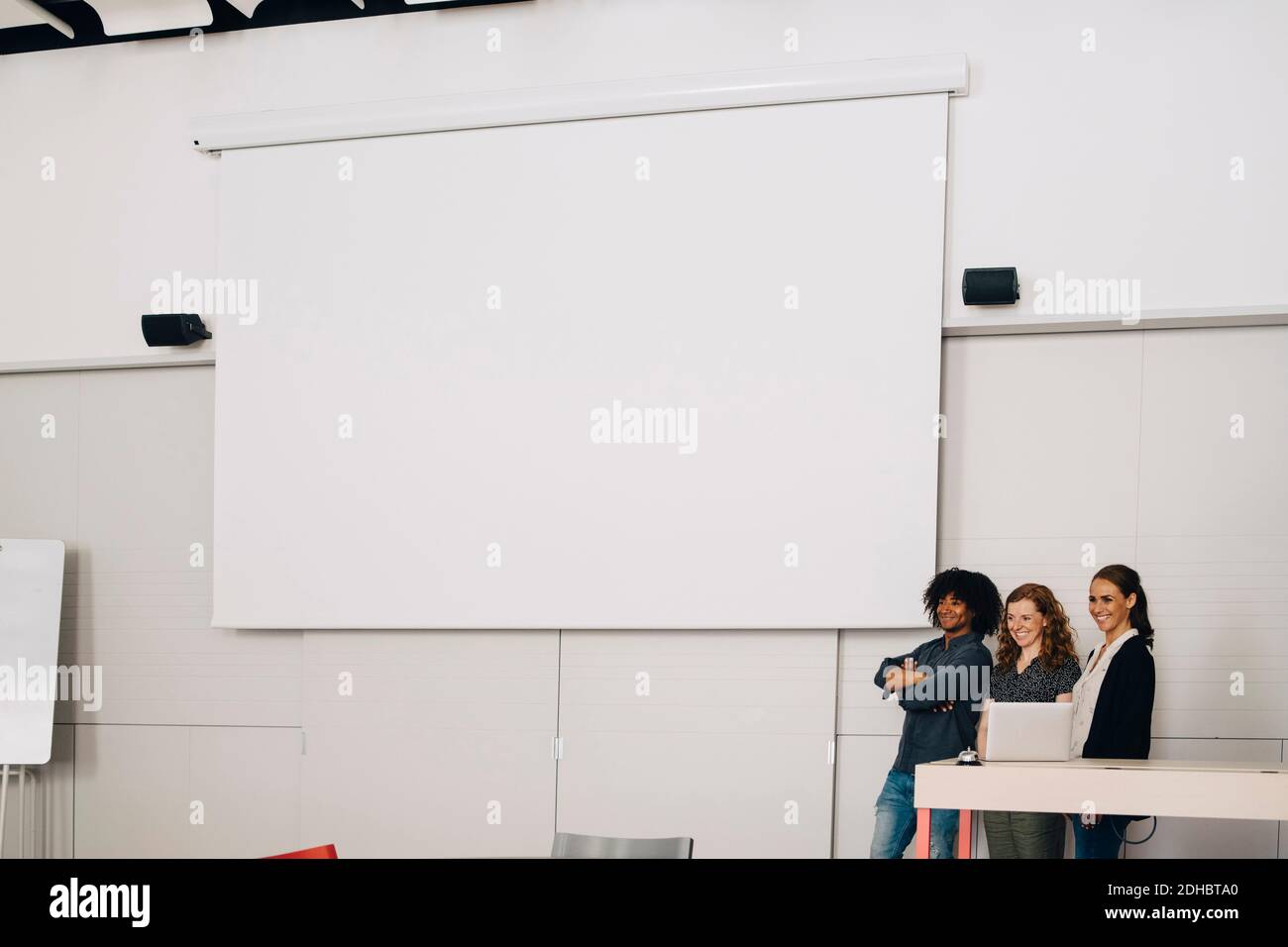 Smiling multi-ethnic technicians standing by blank projection screen at creative office Stock Photo