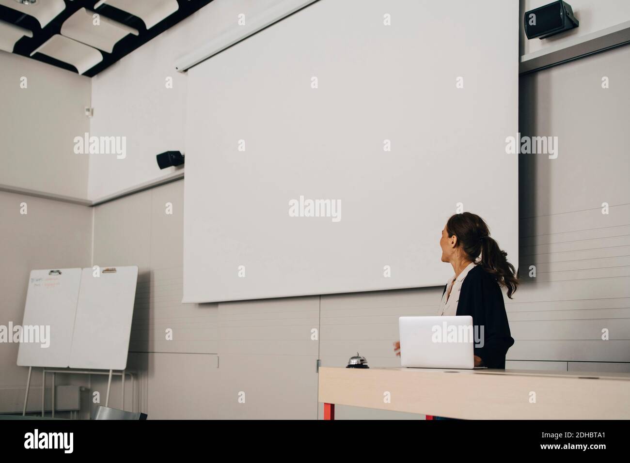 Businesswoman giving presentation while looking at blank projection screen at creative office Stock Photo