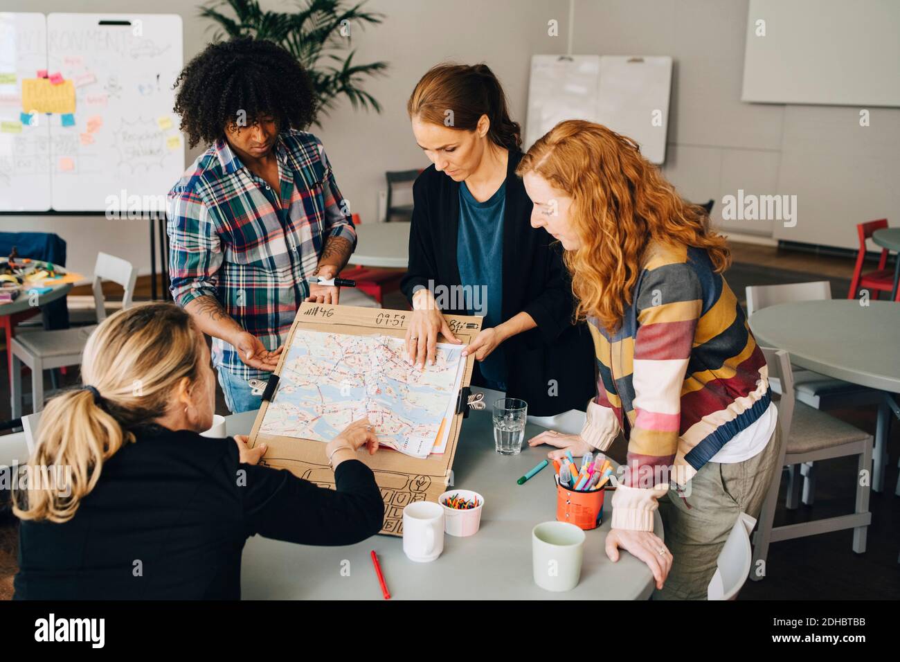 Multi-ethnic students showing map on placard to female manager at table in creative office Stock Photo