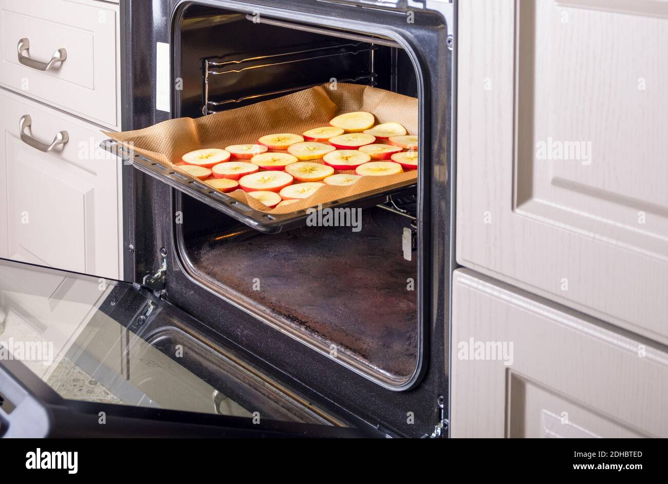 A close-up of a baking sheet with sliced apples stands in an electric oven in a home kitchen. Dried fruits, healthy food. Selective focus. Stock Photo