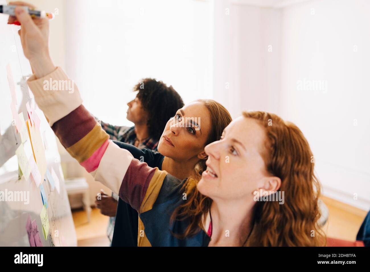 Confident female technicians discussing project over whiteboard by businessman working at creative office Stock Photo