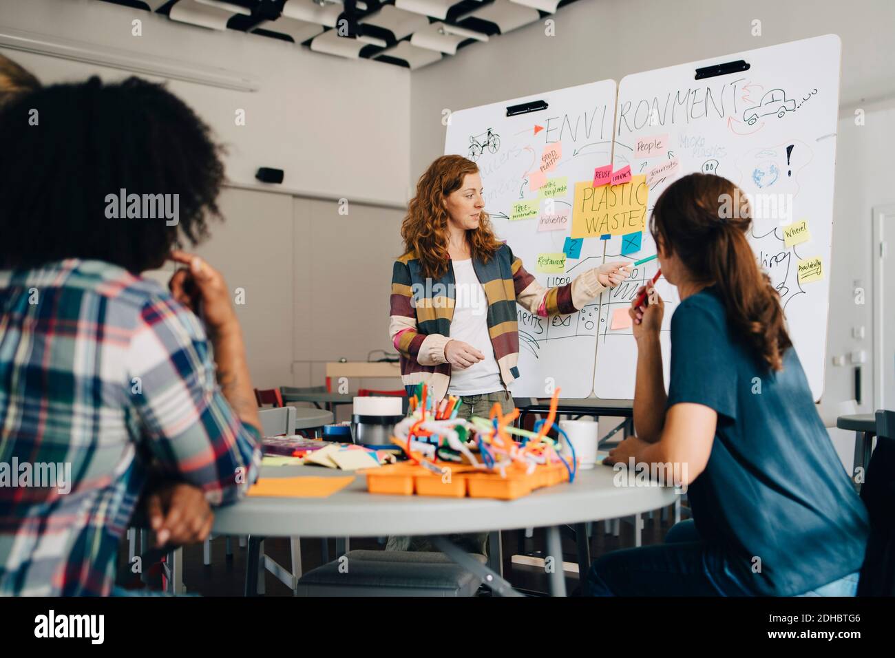 Confident businesswoman explaining plastic waste management plan to technicians over whiteboard at creative office Stock Photo