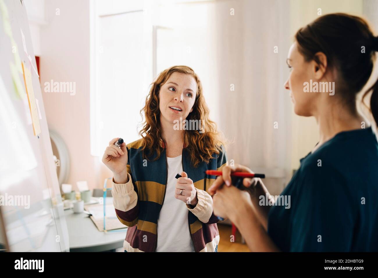 Confident female mid adult students discussing project over whiteboard at creative office Stock Photo