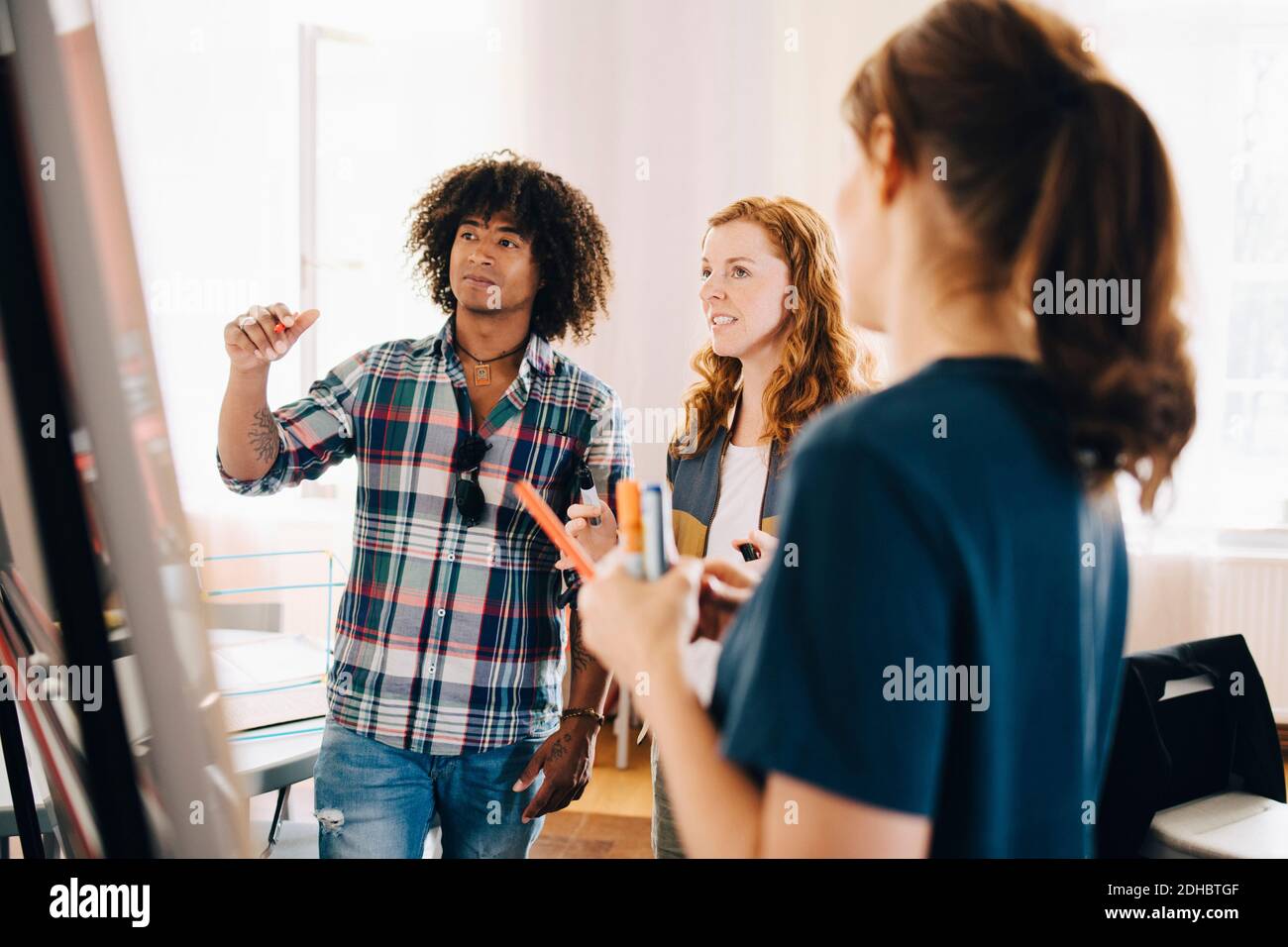 Confident multi-ethnic technicians discussing project over whiteboard at creative office Stock Photo