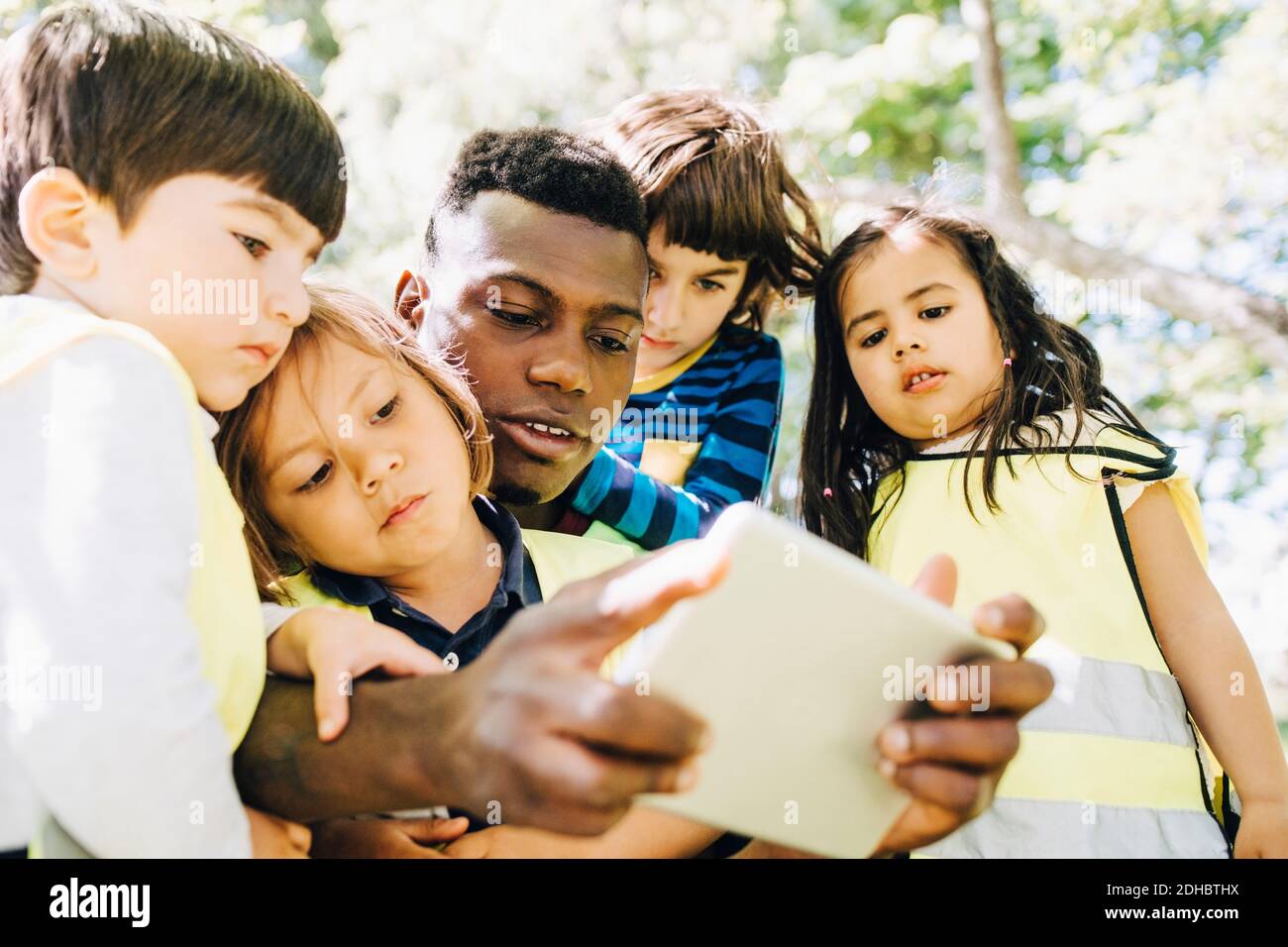 Male mid adult teacher sharing digital tablet with students in playground Stock Photo