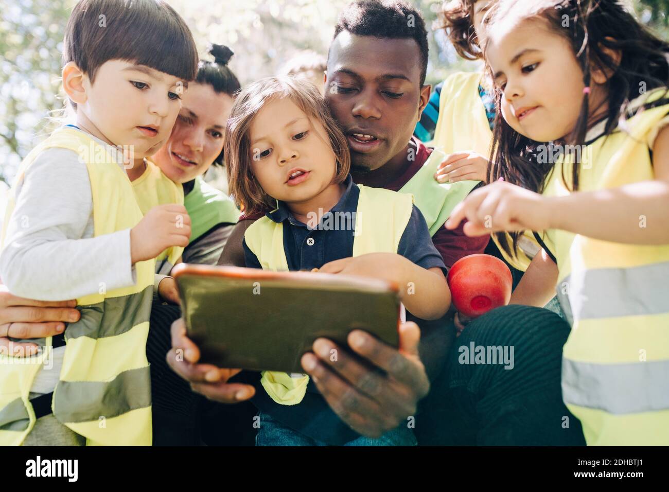 Multi-ethnic students and teachers sharing digital tablet in playground Stock Photo