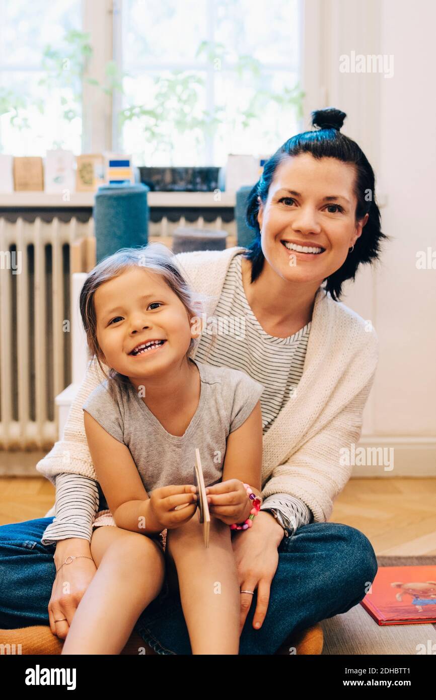 Portrait of smiling girl sitting on teacher's lap in kindergarten