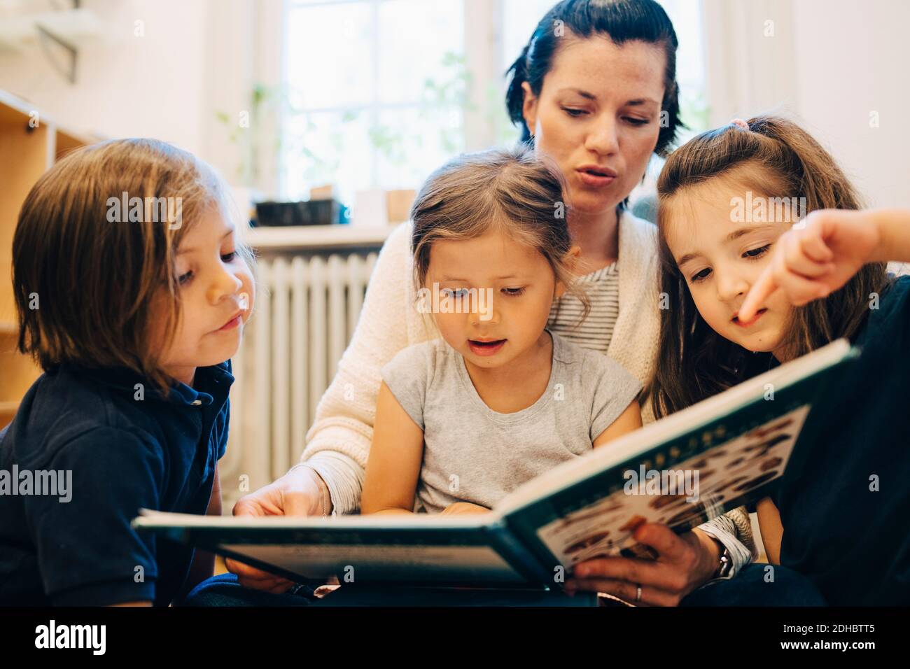 Teacher reading picture book for students in classroom at kindergarten Stock Photo