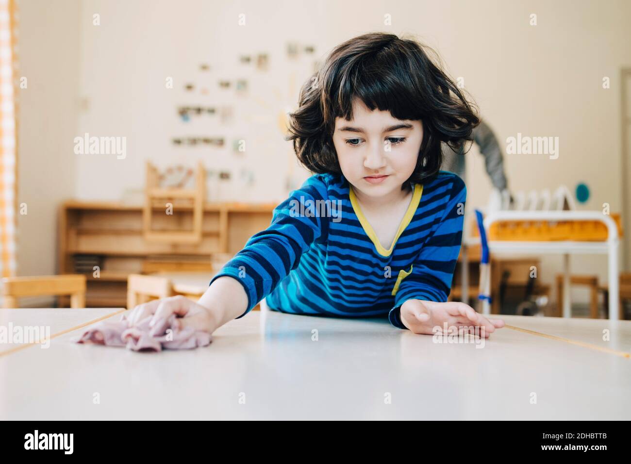 Boy cleaning table with dish cloth in child care classroom Stock Photo