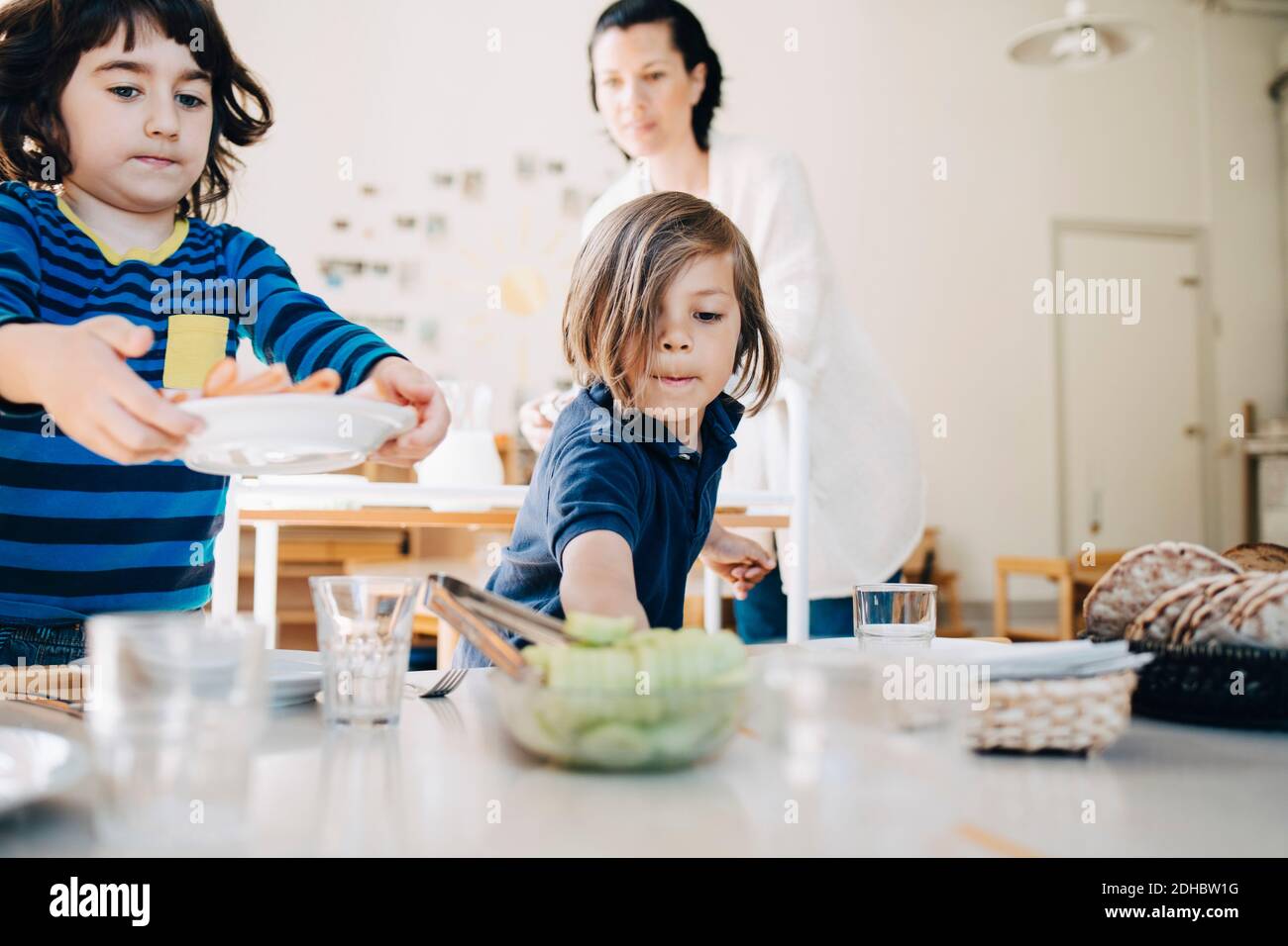 Teacher assisting boys arranging food on table in classroom at child care Stock Photo
