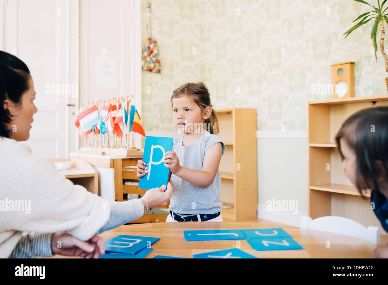Teacher looking at girl holding letter P in classroom Stock Photo