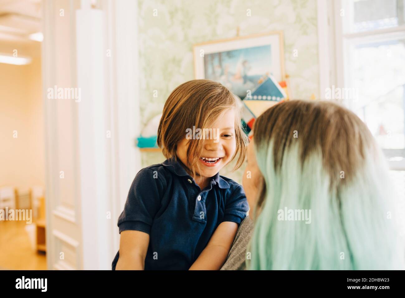 Smiling boy looking at dyed hair teacher in classroom Stock Photo