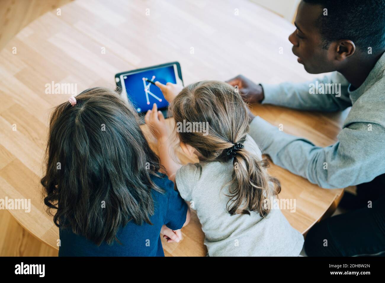 High angle view of girl touching letter K on digital tablet amidst friend and teacher at table in classroom Stock Photo