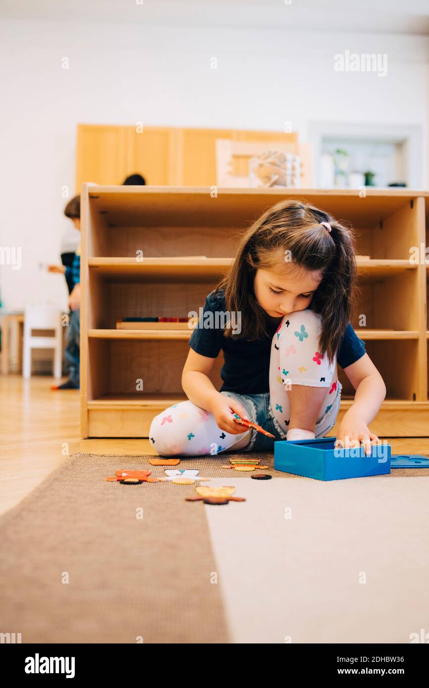 Full length of girl playing with toys while sitting on floor against ...