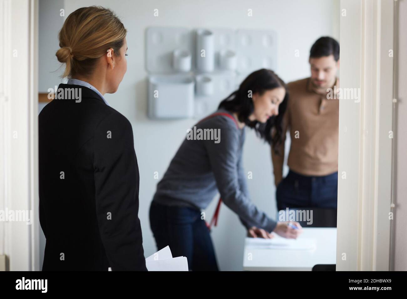 Real estate agent looking at couple signing documents of new house ...