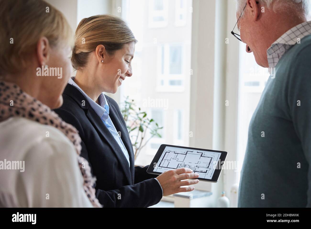 Female real estate agent showing new house blueprint on digital tablet to senior couple at home Stock Photo
