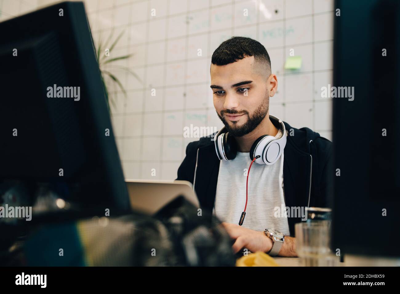 Confident young male computer hacker programming on laptop at creative office Stock Photo