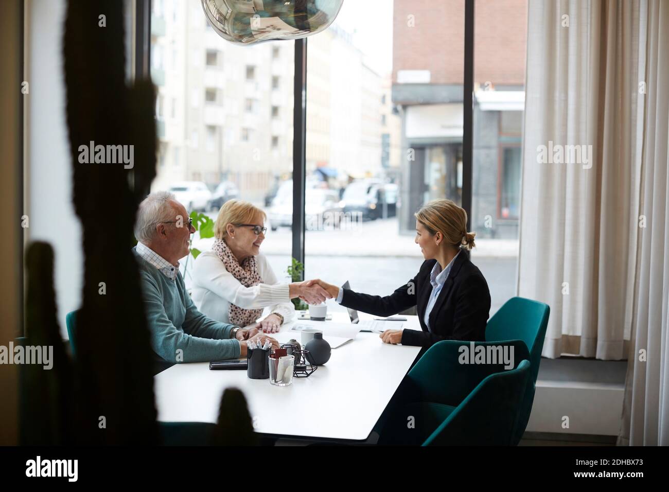 Female estate agent congratulating senior couple for new house at office Stock Photo