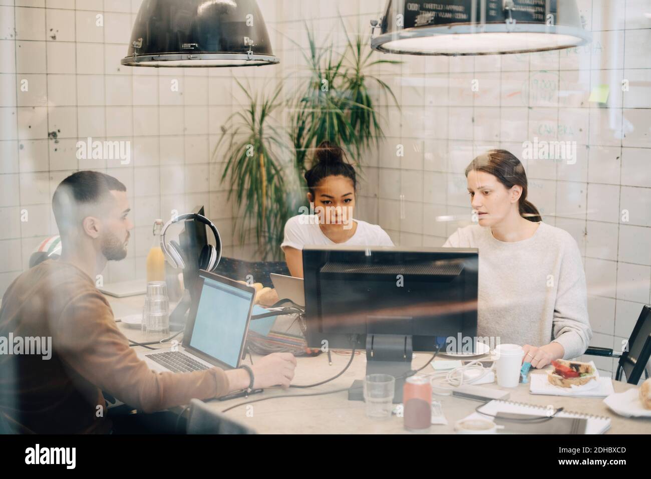Young multi-ethnic computer programmers discussing at creative office seen through window Stock Photo
