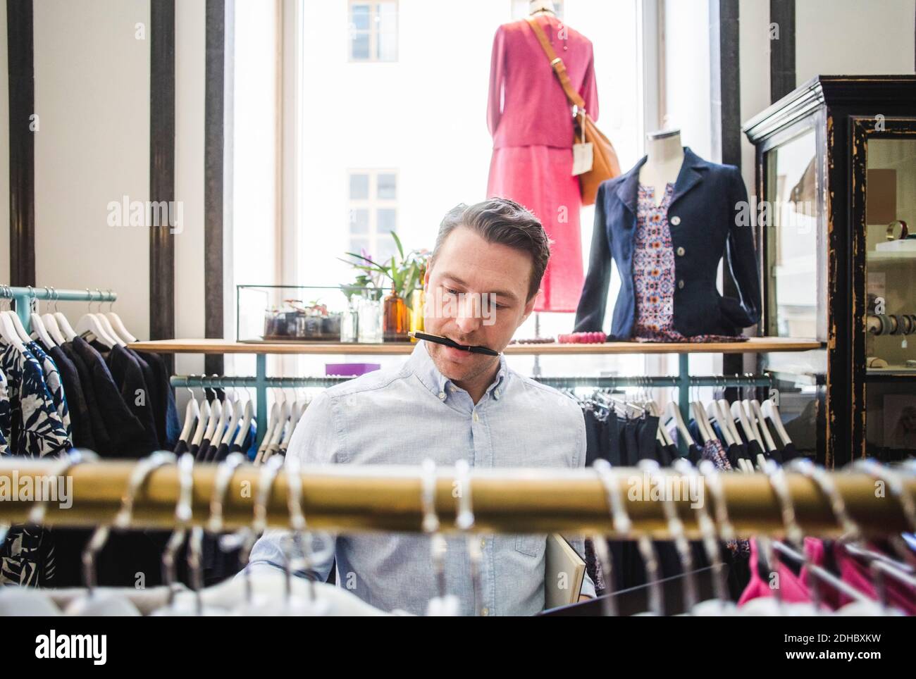 Salesman carrying pen in mouth while looking at clothes rack Stock Photo