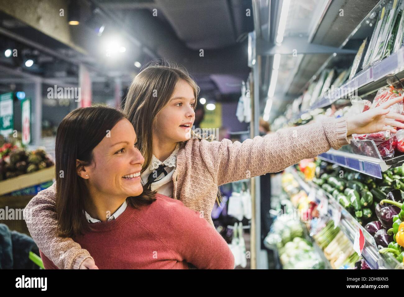 Smiling mother piggybacking daughter while grocery shopping in supermarket Stock Photo