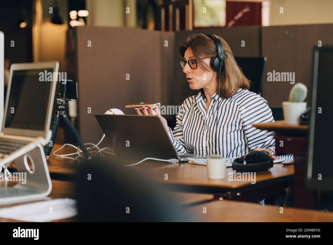 Mature businesswoman wearing headphones while talking on mobile phone ...