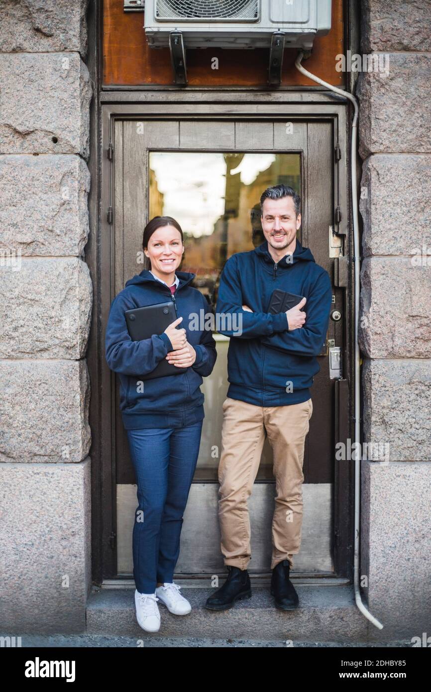 Full length portrait of smiling engineers holding computer equipment while standing outside electronics store Stock Photo