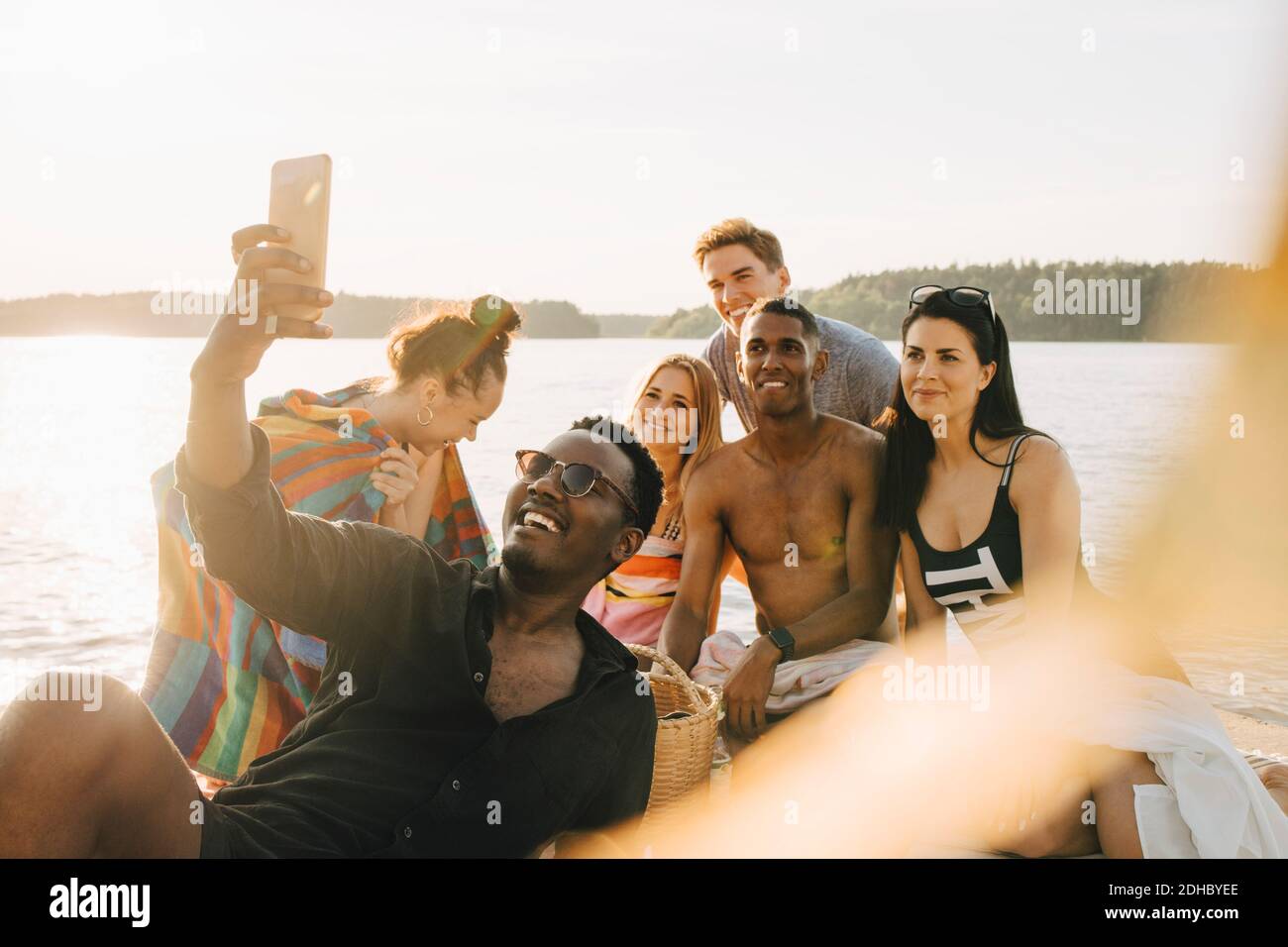 Man taking selfie with happy friends through smart phone on jetty in summer Stock Photo