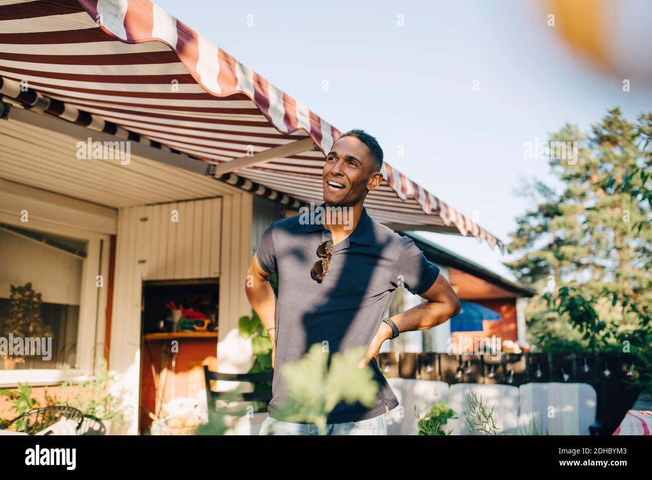 Happy young man looking away while standing with hands on hip at yard Stock Photo