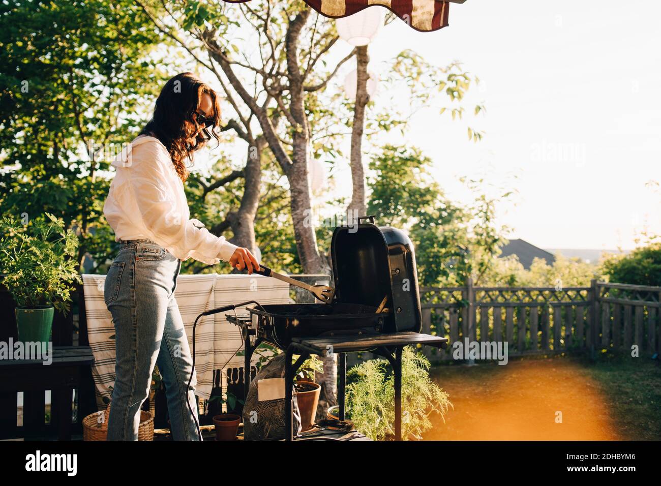 Woman grilling food on barbecue at yard during summer Stock Photo