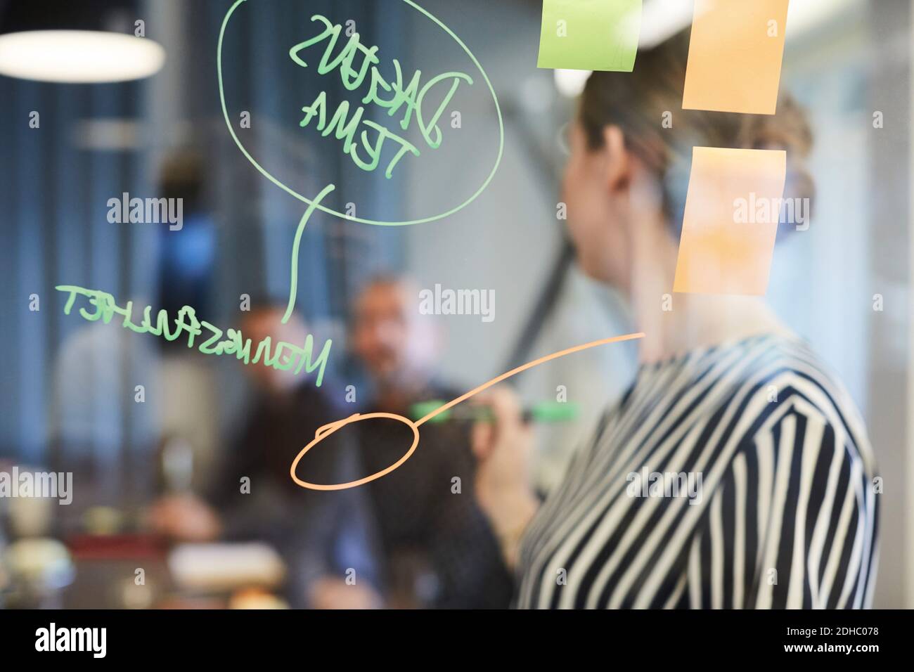 Text and adhesive notes on glass with business people in background at creative office Stock Photo