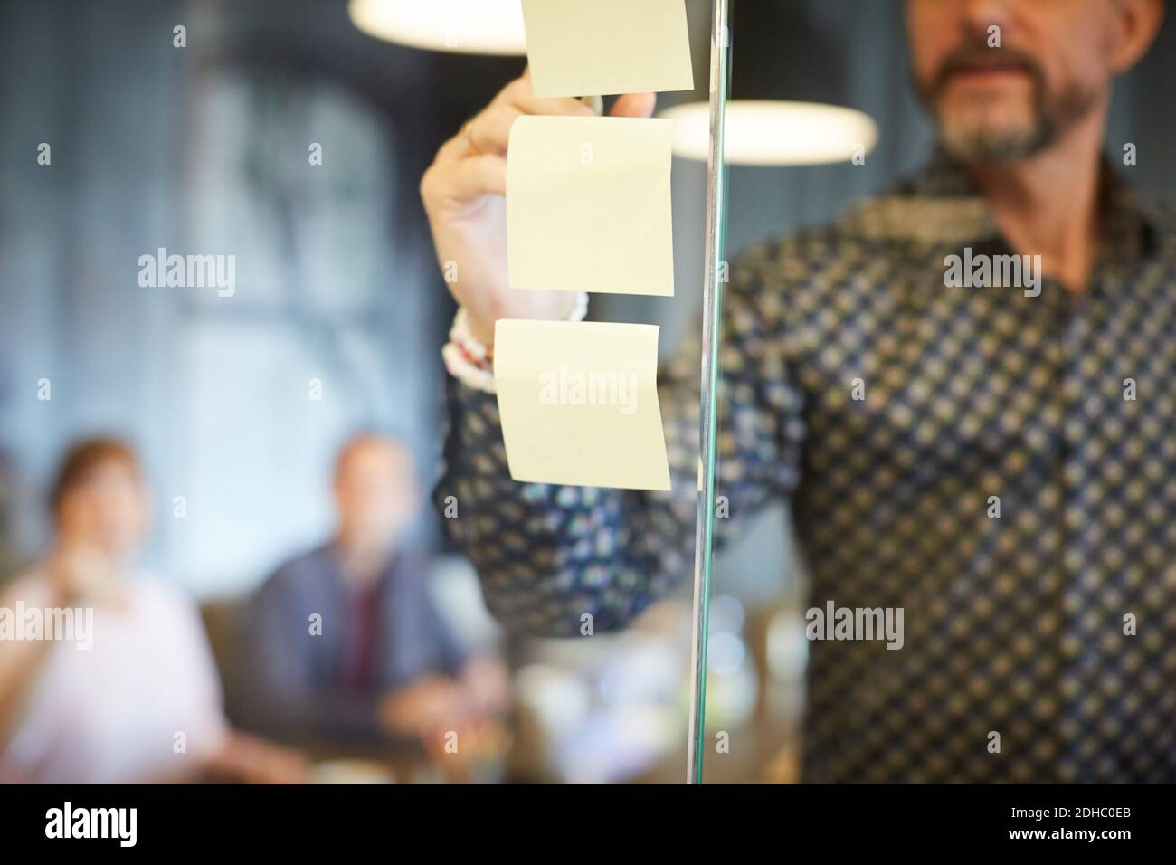 Midsection of businessman writing on adhesive note stuck to glass in creative office Stock Photo