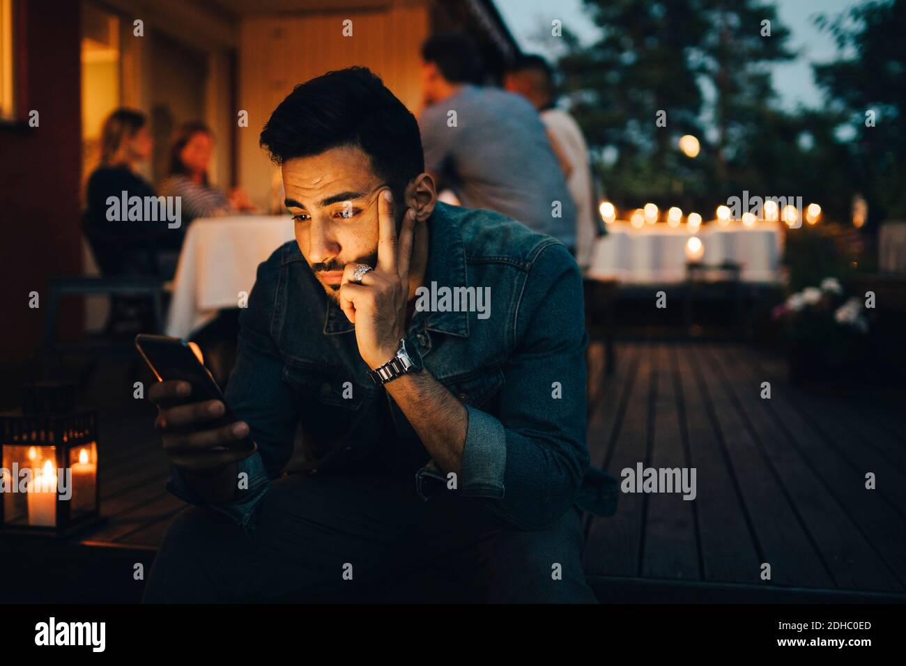 Man using mobile phone while friends in background during dinner party Stock Photo