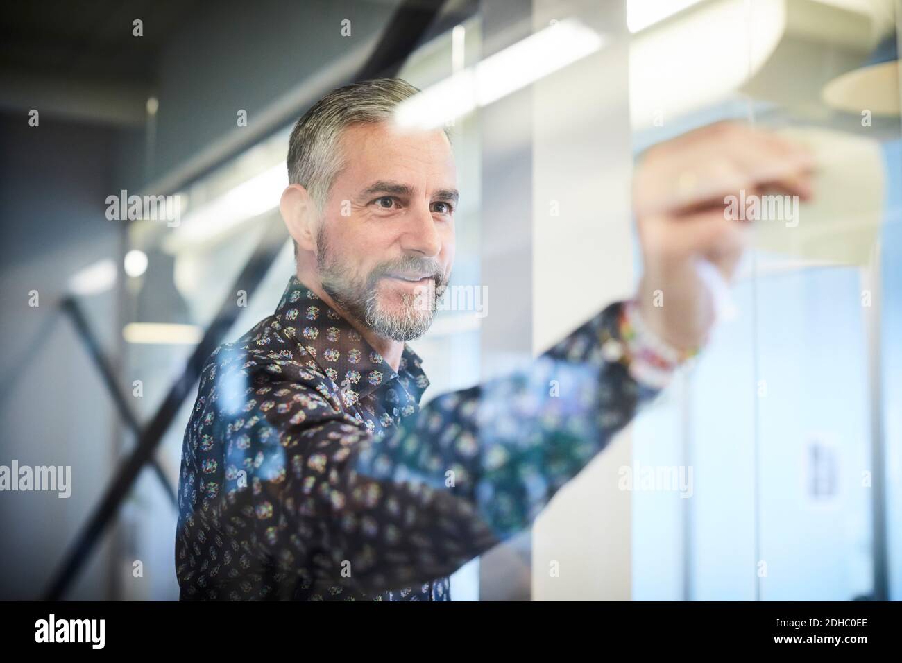 Mature businessman sticking sticky note on glass in board room Stock Photo