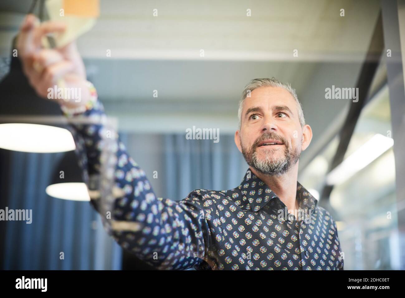 Mature businessman sticking adhesive note on glass in board room Stock Photo